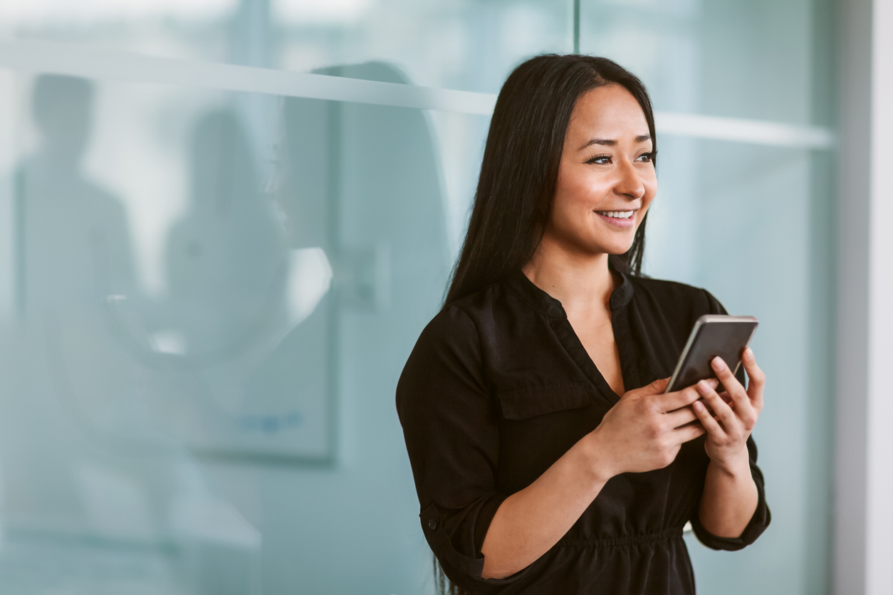 Mixed race multiracial Asian Hispanic Chinese woman texting on phone while looking off to the side in modern business office